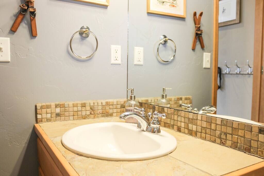 A bathroom with a sink, mirror, and towel rings.