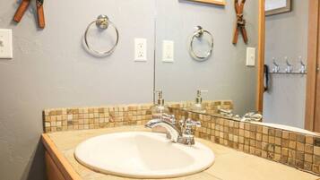 A bathroom with a sink, mirror, and towel rings.