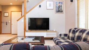 Een woonkamer met een grote flatscreen televisie, een bank, een salontafel en een trap.