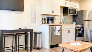 A modern kitchen with white cabinets, stainless steel appliances, a black countertop, and a wooden table. - Aspen Vista Hideaway (Steamboat Springs)