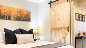 A hotel room with a large bed, a wooden sliding door, a painting of autumn trees, and a small table with a lamp. - Aspen Vista Hideaway (Steamboat Springs)