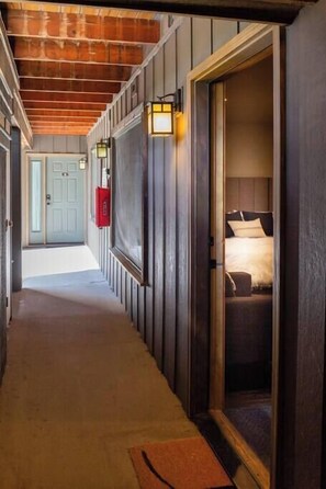 A hallway with wooden beams, a door leading to a room with a bed, and a red mailbox. - Hillside Haven (Steamboat Springs)