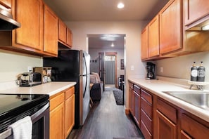 Una cocina estrecha con armarios de madera, un refrigerador negro, un tostador y una cafetera.