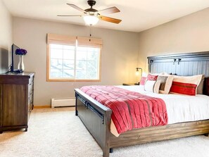 Een slaapkamer met een bed, een plafondventilator, een raam, een dressoir en een nachtkastje.