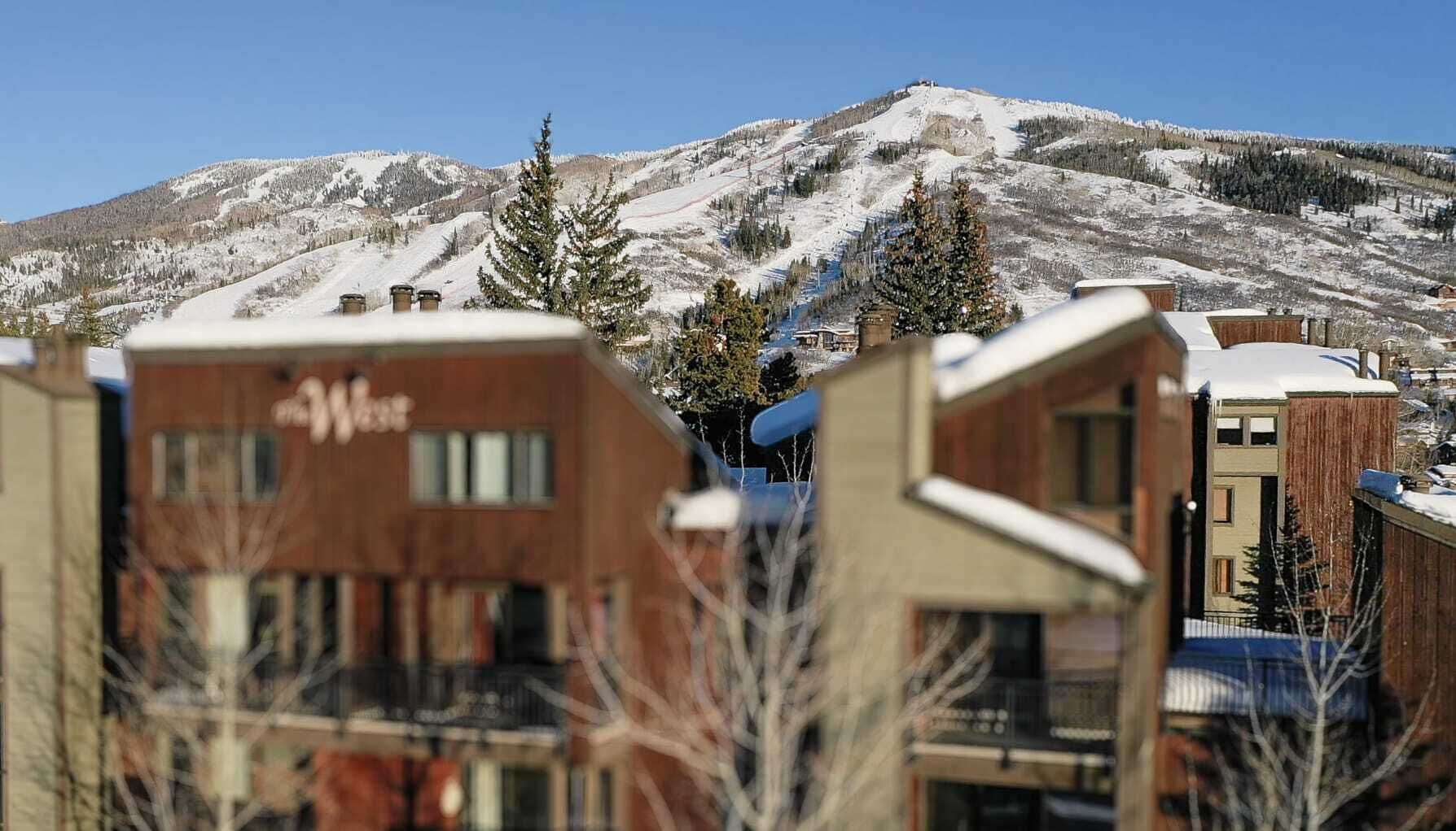 Un edificio moderno con un letrero con la letra 'W', rodeado de montañas y árboles cubiertos de nieve.
