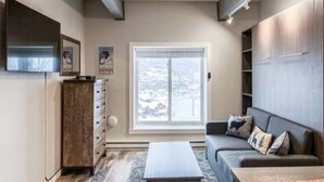 En moderne stue med en sofa, et sofabord og et fjernsyn monteret på væggen.