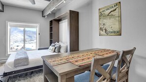 Et moderne værelse med en seng, et spisebord med stole, en ventilator i loftet og et stort vindue med udsigt.