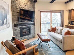 A living room with a stone fireplace, a television mounted above it, a sofa with cushions, and a bench.