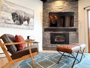 Una sala de estar con chimenea de piedra, televisor montado, sofá y banqueta.