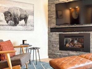 Una sala de estar con chimenea, televisor montado y un cuadro de un búfalo.