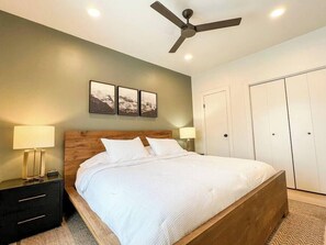Un dormitorio con cama, mesitas de noche, ventilador de techo, armario y cuadros en la pared.
