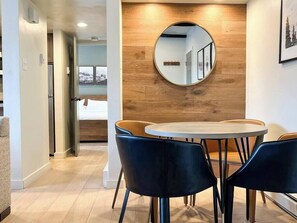 A modern hotel room with a round table, two chairs, a wooden accent wall, and a mirror.