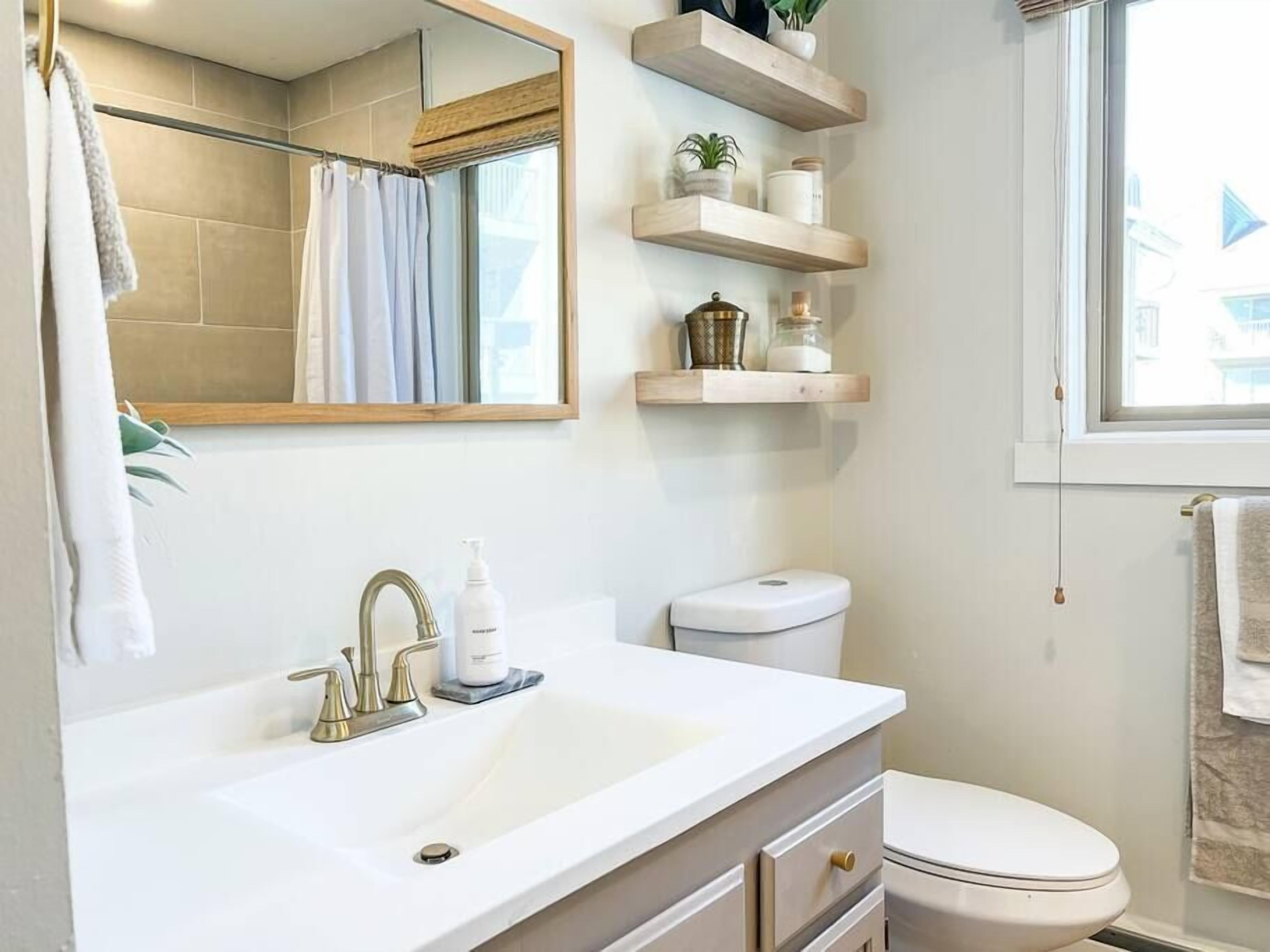 Een badkamer met een witte wastafel, toilet, spiegel en houten planken boven de wastafel.