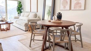 Ein modernes Wohnzimmer mit einem runden Holzesstisch, grau gepolsterten Sesseln und einer großen gewebten Pendelleuchte.