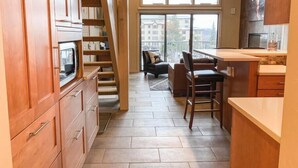 A modern kitchen with wooden cabinets, a built-in microwave, and a dining area with a bar stool. - Slopeside Chalet (Steamboat Springs)