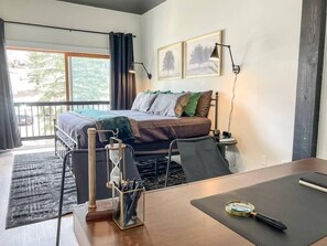A bedroom with a bed, bedside table, lamp, and a view of the outdoors. - Evergreen Escape Summ (Steamboat Springs)