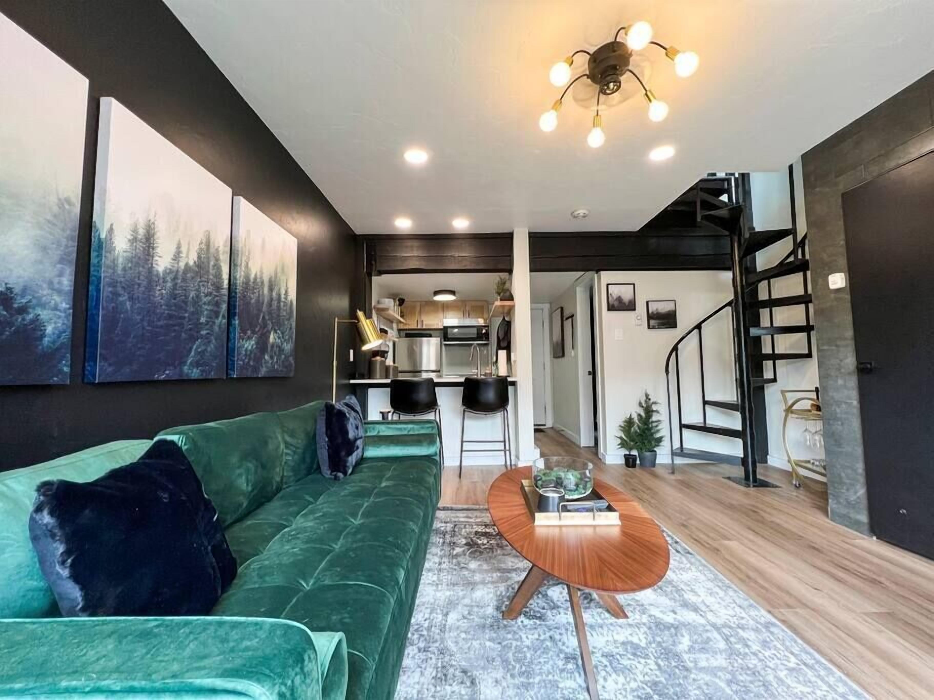 Ein modernes Wohnzimmer mit einem grünen Sofa, einem Holztisch und einer Treppe, die zu einer oberen Ebene führt.