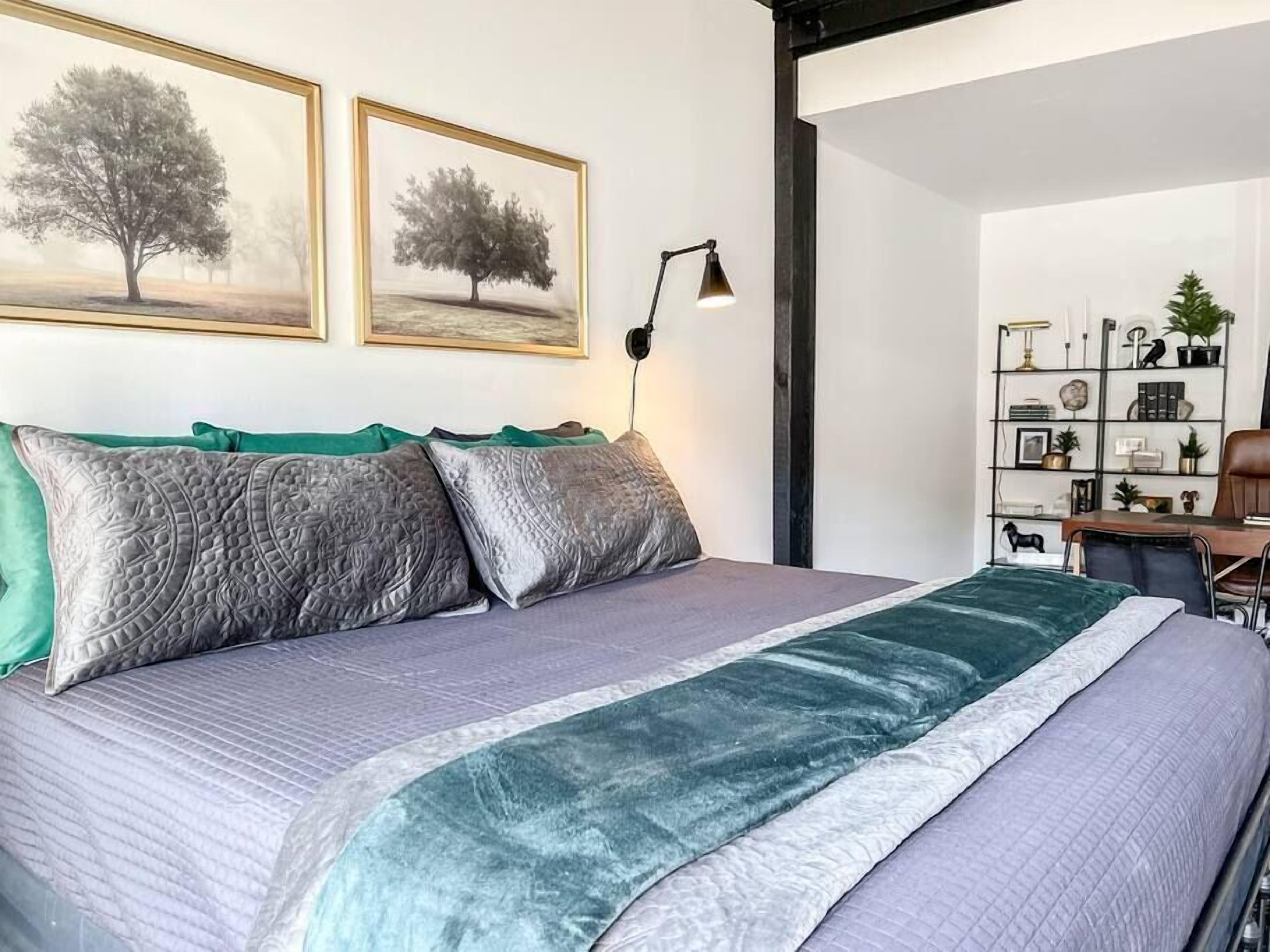 Une chambre à coucher avec un lit, deux tableaux encadrés au mur, un bureau avec une chaise et une bibliothèque.