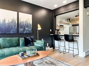 A modern living room with a green sofa, a coffee table, and a kitchen area in the background. - Evergreen Escape Summ (Steamboat Springs)