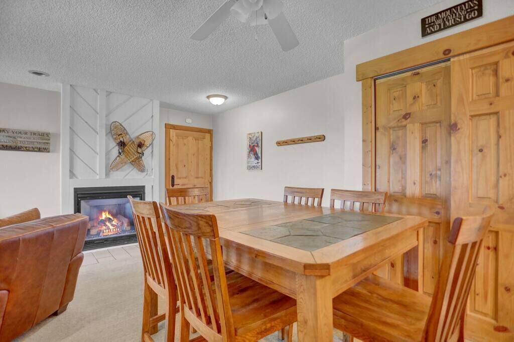 A dining area with a wooden table and chairs, a fireplace, and wooden paneling on the walls.