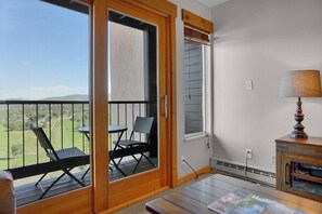 A balcony with two chairs and a table, a lamp, and a view of a green landscape. - Mountain Ridge Retreat (Steamboat Springs)