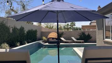 A backyard with a swimming pool, lounge chairs, and string lights.