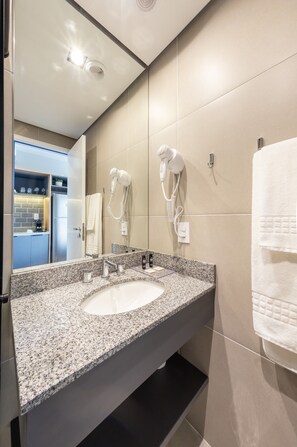 A modern bathroom with a granite countertop sink, a large mirror, a hairdryer, and a towel rack.