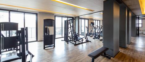 Uma academia moderna com diversos equipamentos de exercício, amplas janelas e piso de madeira.