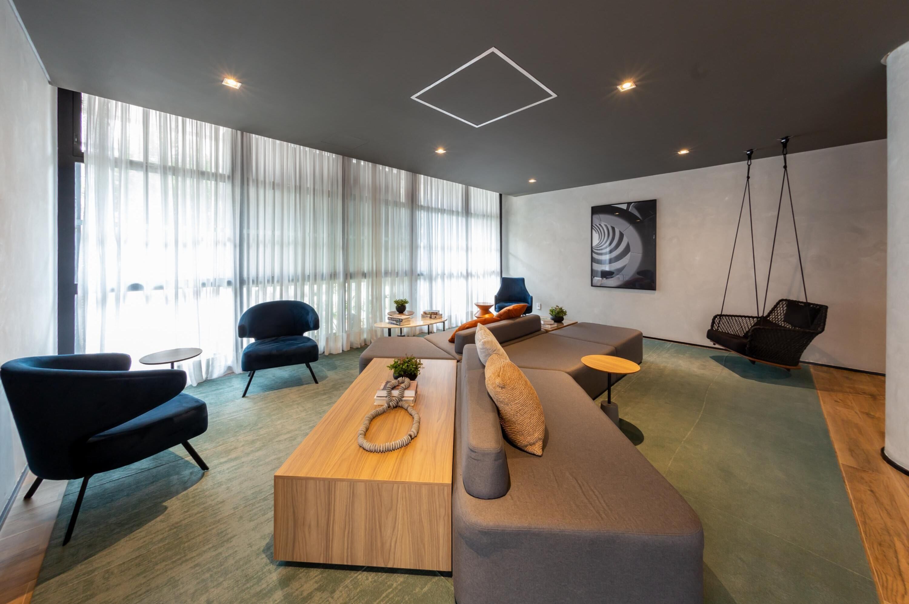 A modern living room with a sectional sofa, a wooden coffee table, and a hanging chair. There are two black armchairs and a small round table with a plant.