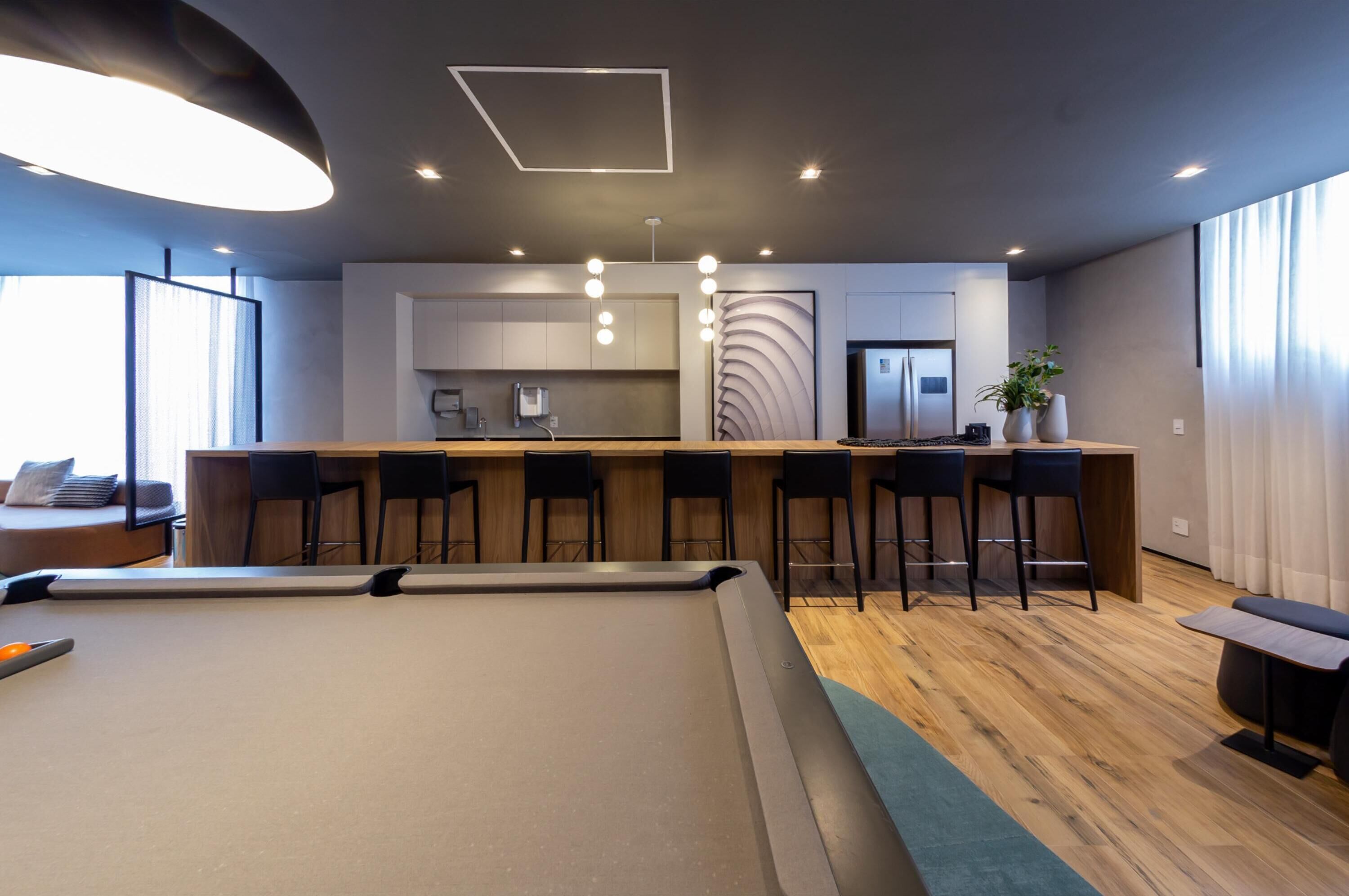 Een moderne woonkamer met een pooltafel, een bar voorzien van krukjes, en een keuken op de achtergrond.