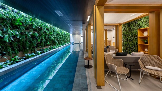 Un espace piscine intérieur moderne, doté d’une longue piscine, de sièges en bois et d’un mur végétal vertical.