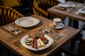 A wooden table with a plate of food, including bread, sausages, and vegetables, and a cup of coffee. - Południk Park Hotel Conference&SPA (Stargard Szczecinski)