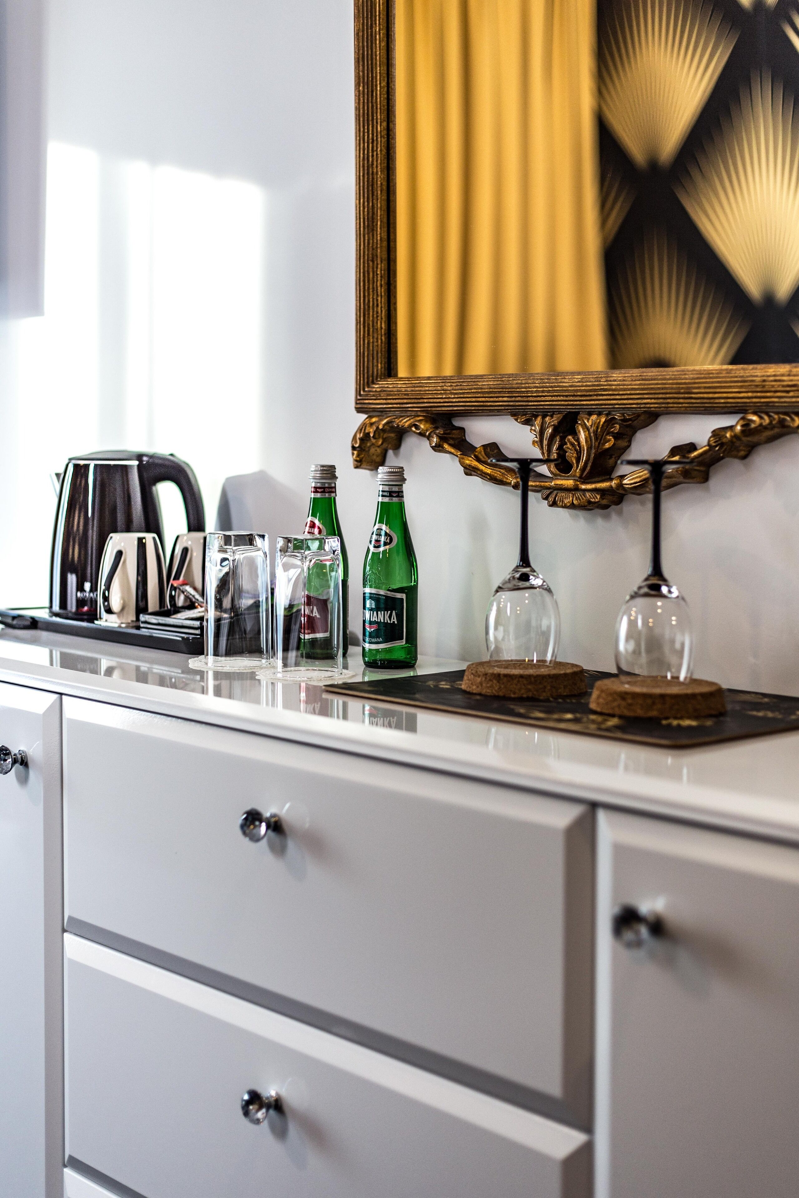 A modern kitchen with a white countertop, a coffee maker, two glasses, and two bottles of beer.