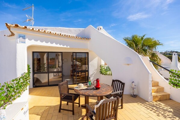 A patio with a table and chairs, a red pitcher, and a white wall with a window. - Villa Veiguinha - Three Bedroom Villa, Sleeps 6 (Vale Rebelho)