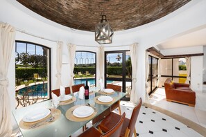 Un coin repas avec une table en verre, des chaises et une vue sur une piscine.