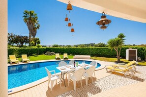 Une piscine entourée d’un jardin aménagé, avec des chaises longues et une table dressée pour les repas.