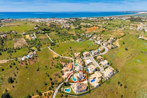 Vue aérienne d’un quartier résidentiel situé sur la côte, avec des maisons, des espaces verts et une vaste étendue d’eau en arrière-plan.