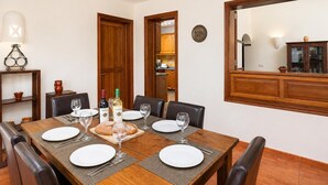 A dining area with a wooden table set for six, surrounded by chairs. There is a bottle of wine and a loaf of bread on the table. - Villa Capricho - Three Bedroom Villa, Sleeps 6 (Montaña Roja)