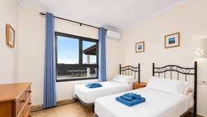 A hotel room with two beds, a wooden dresser, a window with curtains, and a view of the outside. - Villa Capricho - Three Bedroom Villa, Sleeps 6 (Montaña Roja)
