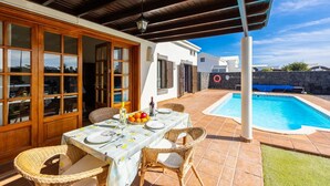 A covered patio with a dining table set for two, a pool, and a stone wall. - Villa Capricho - Three Bedroom Villa, Sleeps 6 (Montaña Roja)