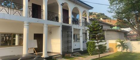A two-story building with a white facade, multiple balconies, and a car parked in the driveway.