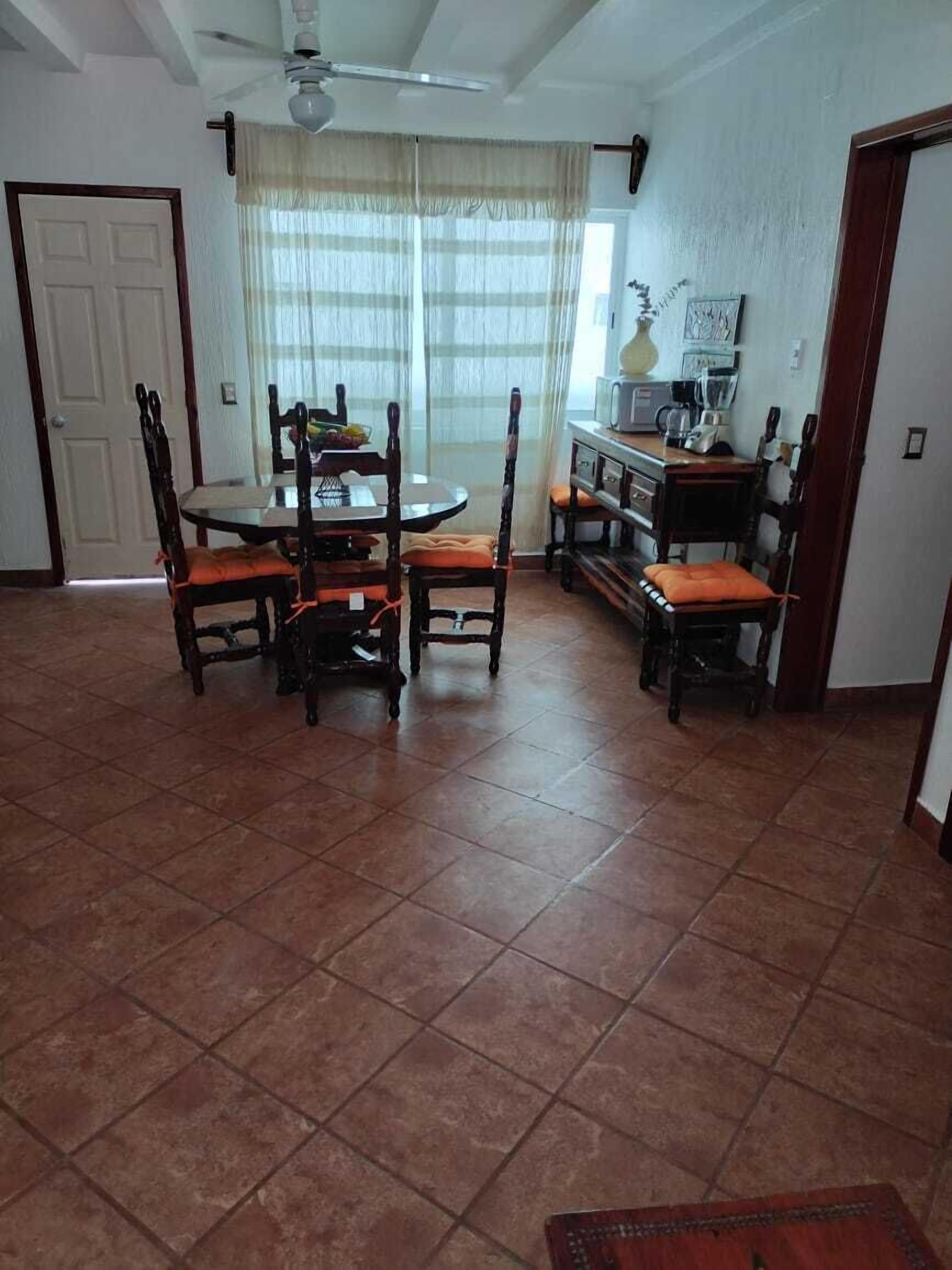 A dining area with a round table and six chairs, a ceiling fan, and a kitchen area with a microwave and coffee maker.