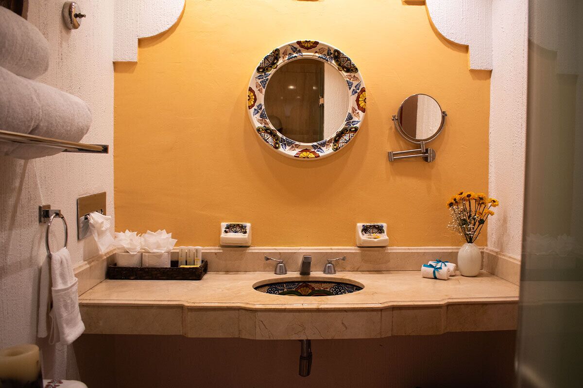 A bathroom with a sink, two mirrors, a towel rack, and a vase with flowers.