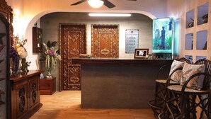 Un área de recepción con un mostrador de madera, un televisor montado en la pared y un espacio de descanso con sillas de mimbre.