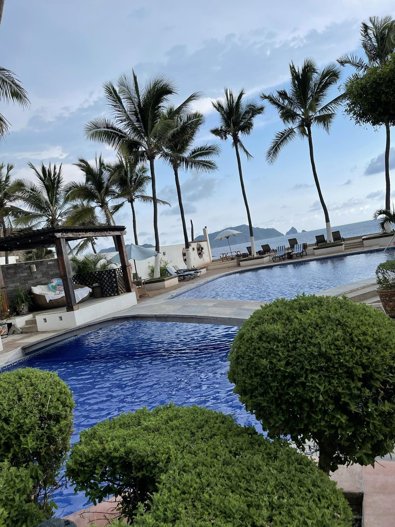 Zona de piscina con palmeras, sillas de descanso y vista al océano.