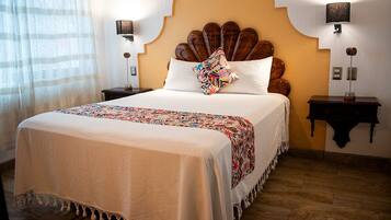 A hotel room with a large bed, a wooden headboard, two bedside tables with lamps, and a window with sheer curtains.