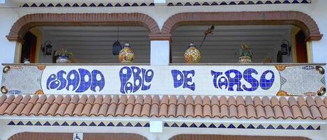 Un edificio de dos plantas con techo de tejas, un balcón con un letrero y una entrada cubierta.