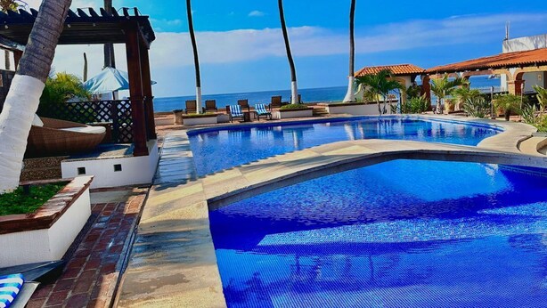 Piscina de resort con palmeras y un cielo azul despejado.