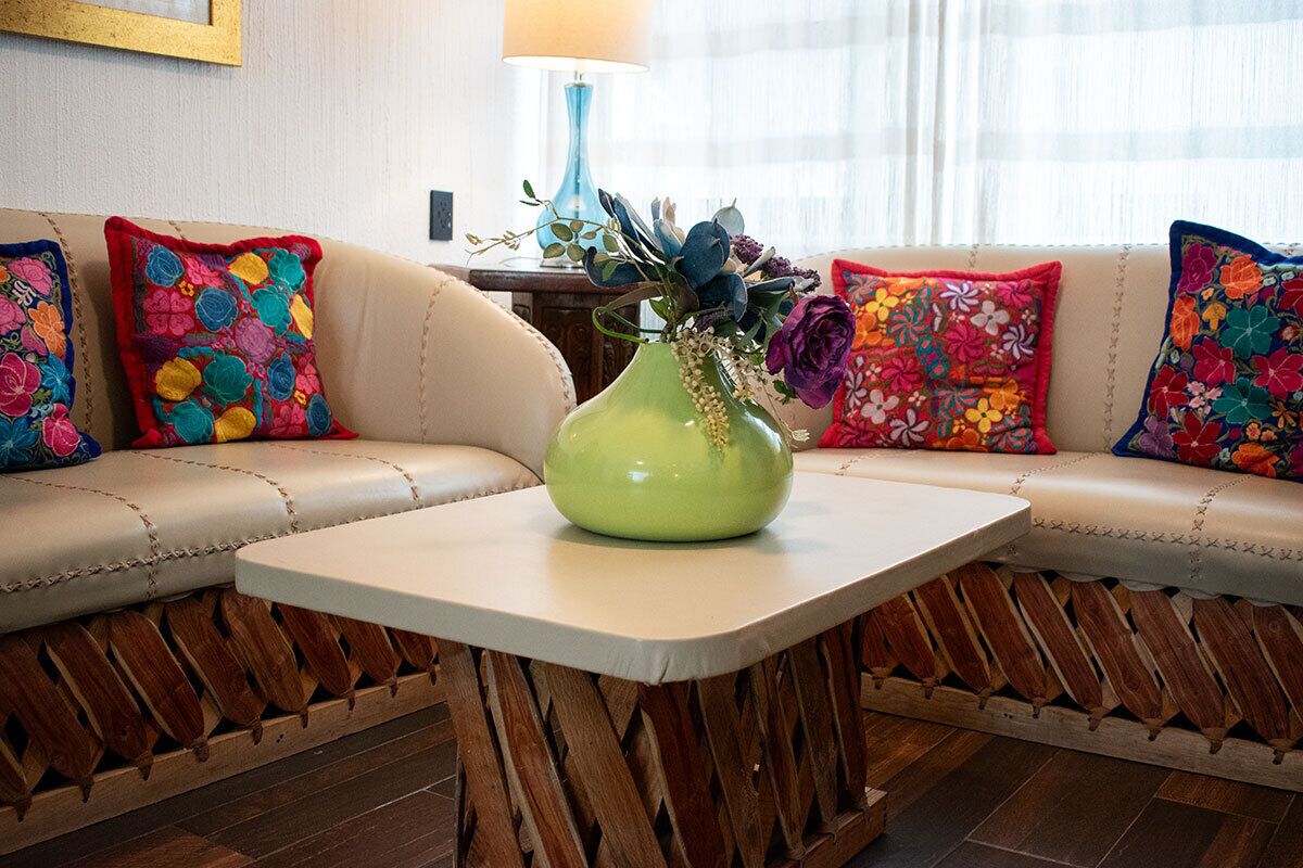 Una sala de estar moderna con un sofá color crema, almohadones bordados de colores, un jarrón verde con flores y una mesita de madera.