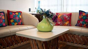 Una sala de estar moderna con un sofá color crema, almohadones bordados de colores, un jarrón verde con flores y una mesita de madera.